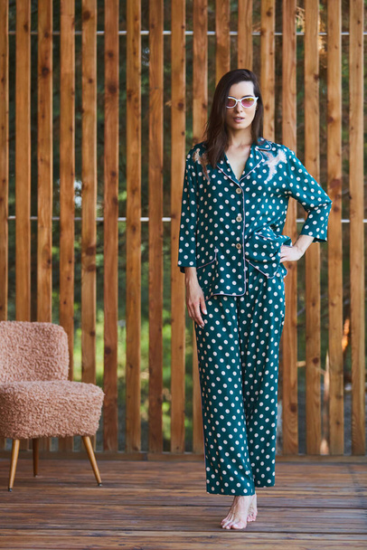 Woman standing in pajamas pajamas with polka dots on wooden background in full length. Caucasian female model. - Фото, зображення