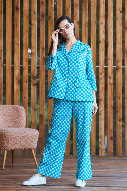 Woman standing in pajamas pajamas with polka dots on wooden background in full length. Caucasian female model. - Valokuva, kuva