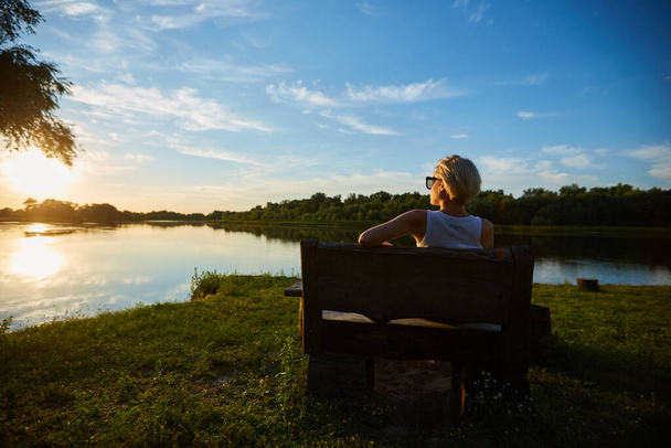 Woman Sitting On Bench During A Beautiful Sunset - 写真・画像