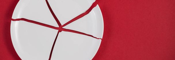 Zerbrochene Teller oder zerbrochenes Wasserglas auf dem roten Hintergrund Das Konzept von Unfällen in der Küche ist gefährlich für den Körper und kleine Kinder im Haus. - Foto, Bild