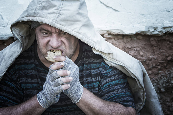 A homeless, toothless, hungry man greedily eats a piece of bread. Poverty, unemployment, hunger. Portrait. Close up. - Photo, image