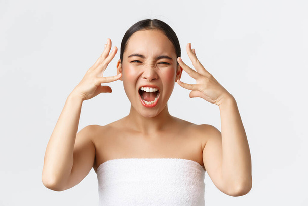 Beauty, cosmetology and spa salon concept. Close-up of outraged, mad distressed asian woman in bath towel screaming and shaking hands near head, feeling furious after bad service in beauty clinic - Photo, Image