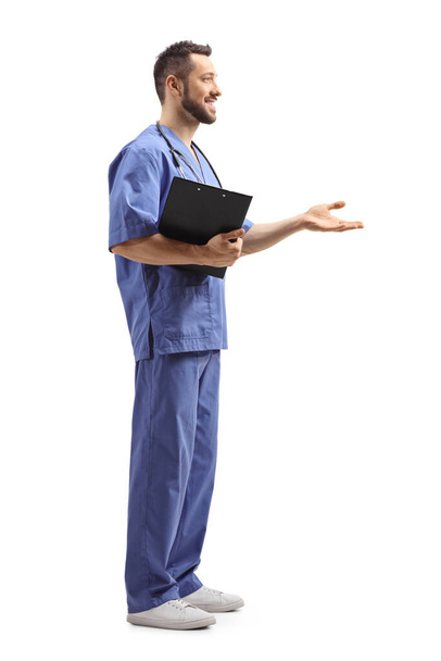 Full length profile shot of a male doctor in a blue uniform gesturing with hand isolated on white background - Φωτογραφία, εικόνα