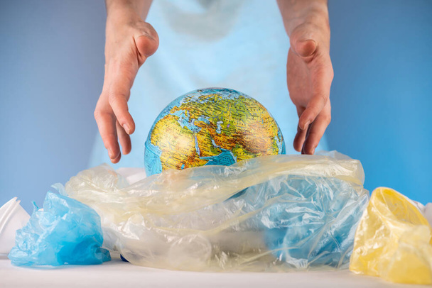 Μια γυναίκα βγάζει μια Γη σε μορφή σφαίρας από ένα σωρό πλαστικά σκουπίδια. Έννοια της περιβαλλοντικής ρύπανσης και τη διάσωση του πλανήτη - Φωτογραφία, εικόνα