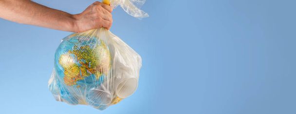 A person is holding a garbage bag with Earth in the form of a globe and plastic in his hand. Concept of environmental pollution and saving the planet - Фото, изображение