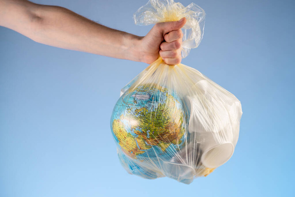 Uma pessoa está segurando um saco de lixo com a Terra na forma de um globo e plástico em sua mão. Conceito de poluição ambiental e salvamento do planeta
 - Foto, Imagem