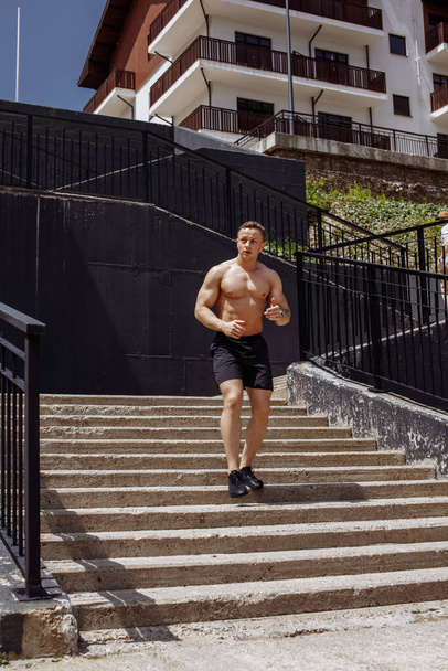 Caucasian shirtless athletic runner running up and down the stairs in the city. - Foto, afbeelding