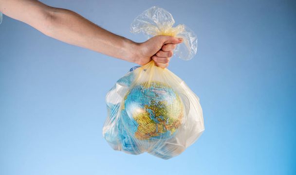 A person is holding a garbage bag with Earth in the form of a globe and plastic in his hand. Concept of environmental pollution and saving the planet - Foto, Bild