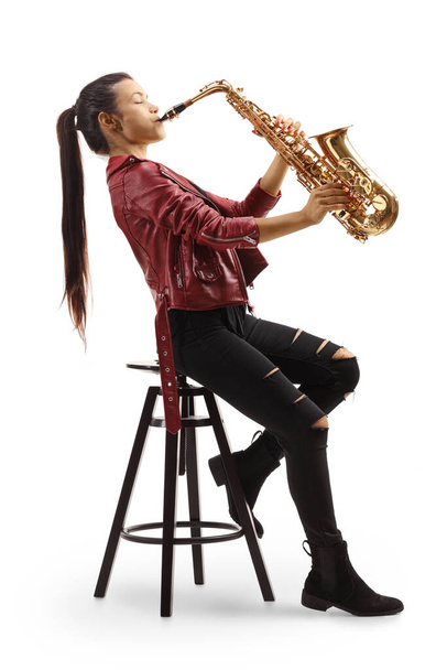 Full length portrait of a beautiful young woman sitting on a chair and playing a saxophone isolated on white background - Foto, imagen