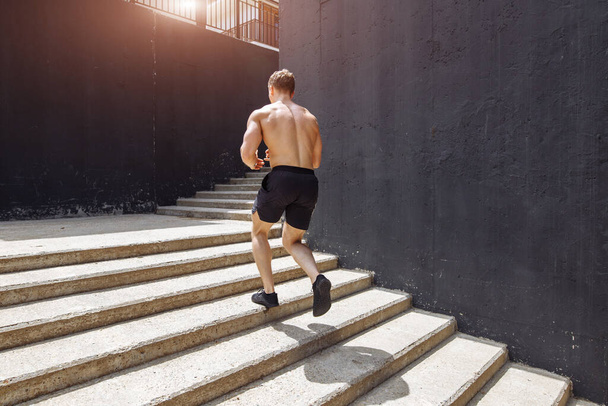 Caucasian sportsman running upwards with energy on the urban staircase - Foto, Imagen