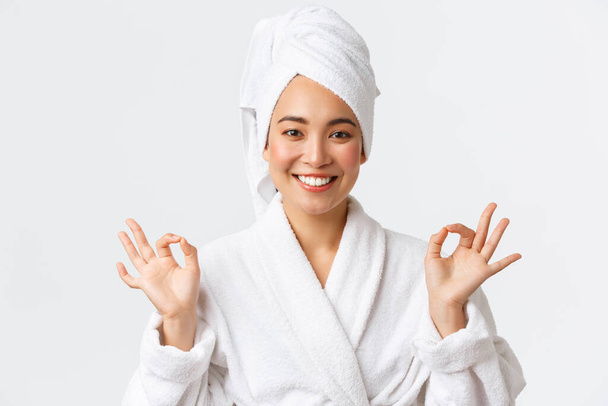 Personal care, women beauty, bath and shower concept. Close-up of relieved attractive asian woman attend spa beauty salon, wear bath towel and bathrobe, meditating, feeling nirvana, smiling - Fotoğraf, Görsel