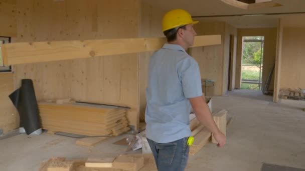 Κοντινό πλάνο Νεαρός ξυλουργός μεταφέρει μια μακριά ξύλινη σανίδα σε όλο το σύγχρονο σπίτι CLT - Πλάνα, βίντεο
