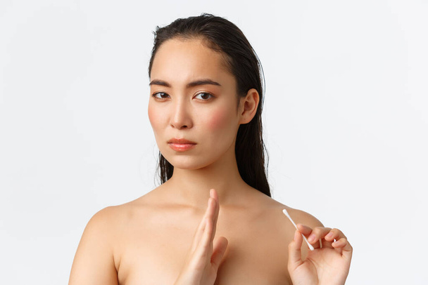 Skincare, women beauty, hygiene and personal care concept. Displeased serious-looking asian female standing naked and turn away from cotton bud, make stop or disapprove gesture, white background - Photo, Image