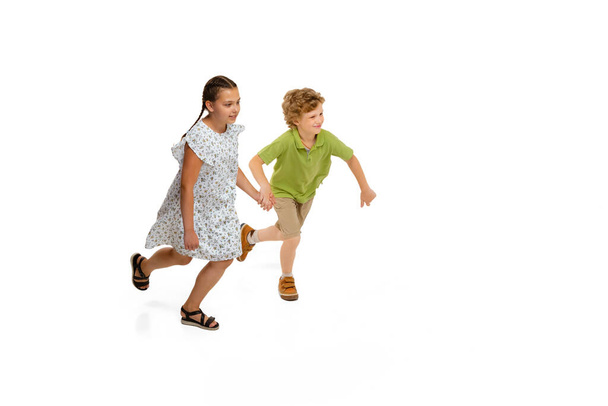 Happy little caucasian girl and boy jumping and running isolated on white background - Zdjęcie, obraz