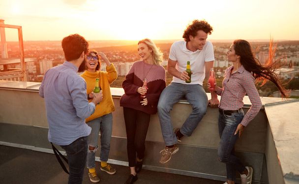 Fröhliche junge Freunde mit Drinks feiern auf dem Dach - Foto, Bild