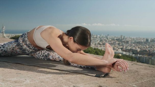 Mujer haciendo retorcido cabeza a rodilla posar al aire libre. Entrenador de ejercicio en la ciudad
 - Foto, Imagen