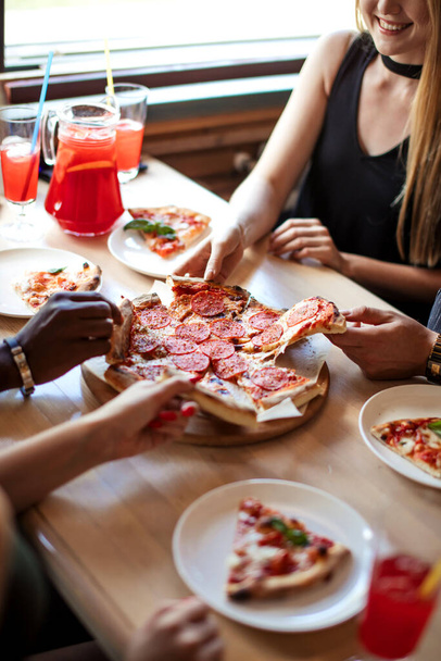 Close-up of people hands taking slices of pepperoni pizza in cafe, top view. - Photo, Image