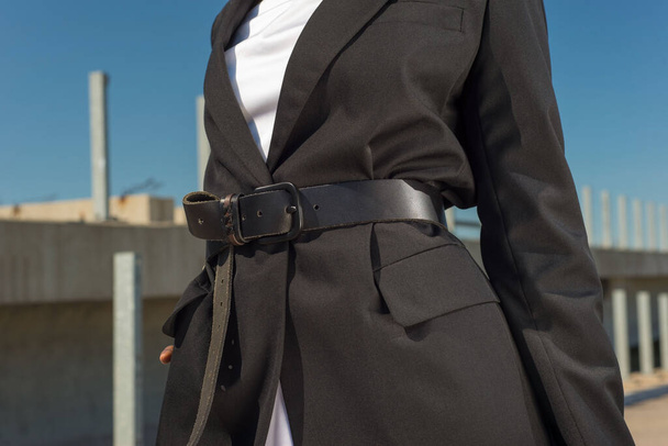 close-up details of a female business black jacket, on a waist a leather belt on an African fashion model, against a blue sky. Style, design of women's clothing. Black fashion girl. Model afro american girl demonstrates a new fashion wearing a belt a - Foto, Imagem