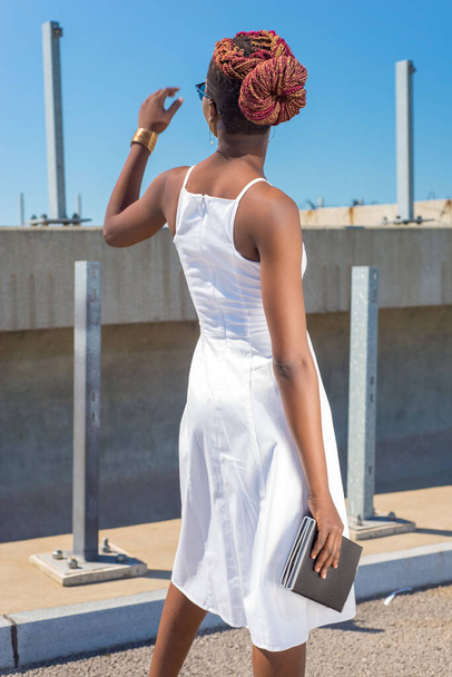 moda menina negra africana em um vestido branco, modelo posando em um fundo de céu azul. Jovem modelo de menina americana africana em vestido branco com costas abertas posando contra o céu azul Sexy mulher afro-americana em vestido curto - Foto, Imagem