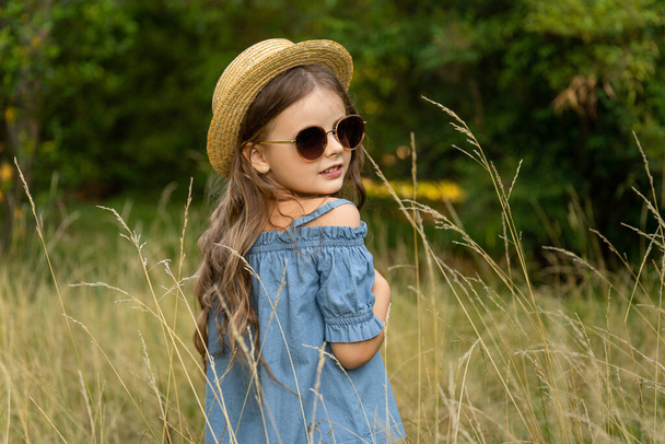 A little girl walking across a field in a straw hat. Children's eco-tourism. Child's vacation in the country - Foto, imagen