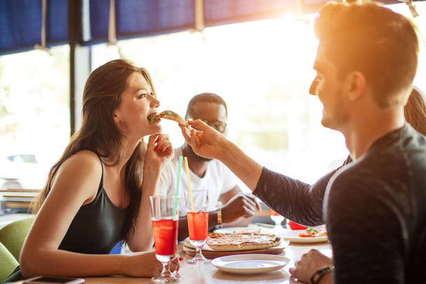 Young diverse friends couple feeding each other with pizza during brunch at cafe - Foto, Imagem