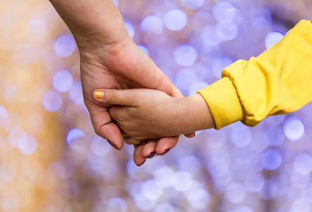 A woman's hand holding the hand of a little girl against the background of bokeh - 写真・画像