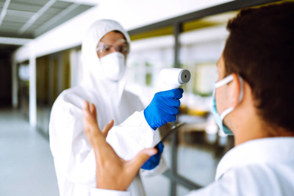 Disease control expert with an Infrared thermometer equipment to check the temperature at office during the coronavirus pandemic. Covid-19.  - 写真・画像