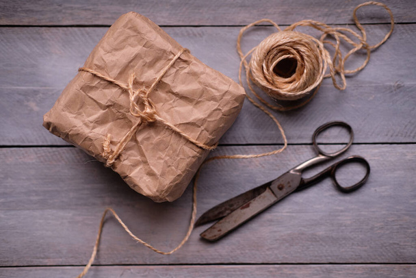 Geschenkpaket aus Kraftpapier, Seil und Schere auf rustikalem Holztisch - Foto, Bild