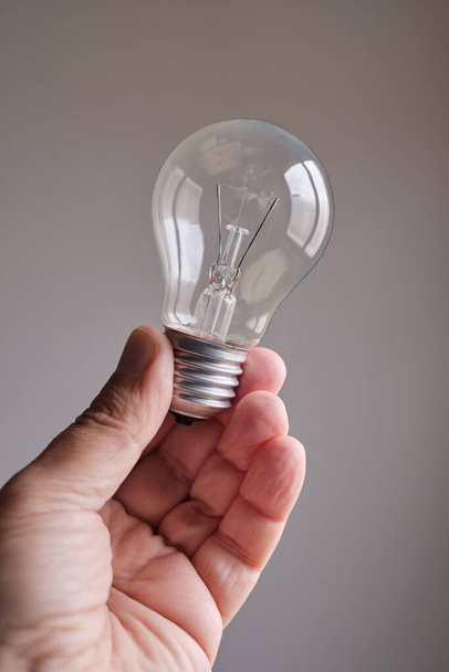 Man's hand holding a light bulb with gray background - Fotografie, Obrázek