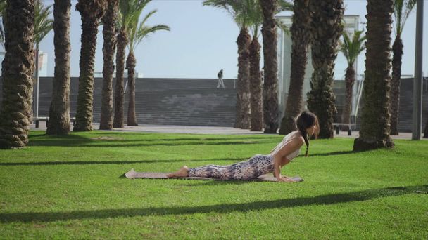 Тренер по йоге делает позу кобры в парке. Женщина занимается йогой на зеленой траве - Фото, изображение