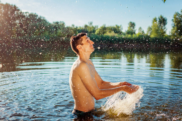 Young handsome man making splashes in river. Guy having fun in water. Summer vacation activities - Foto, imagen