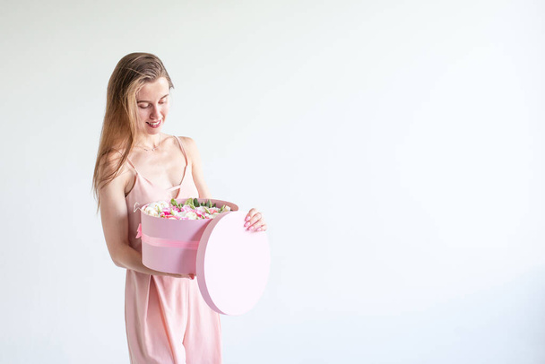 Menina sorridente segurando caixa redonda rosa com flores, macarons franceses e top em mãos no fundo branco.Mulher recive present.Florist fazer romântico, lux buquê de noiva de rosa.Decoração de casamento
 - Foto, Imagem