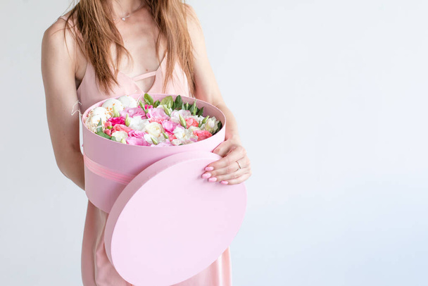 Close up of girl holding round pink box with flowers,french macarons and top in hands on the white background.Woman recive present.Florist make romantic,lux bridal bouquet of roses.Wedding decor - Photo, Image