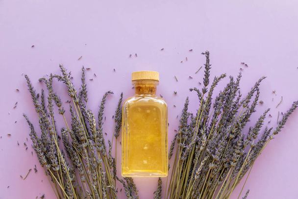 Ätherisches Lavendelöl, eine Flasche und Lavendelstrauß auf violettem Hintergrund - Foto, Bild