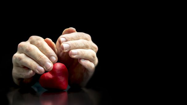Uomo che si cuce le mani protettivamente su un cuore
 - Foto, immagini