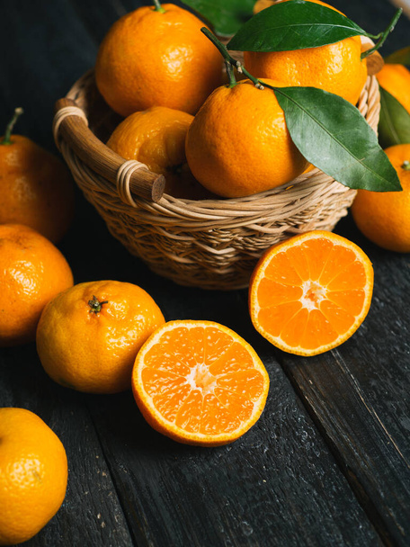 Juicy bright ripe tangerines in wooden basket on dark background - Photo, Image