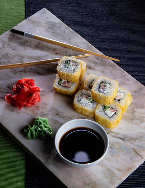 Sushi. Uma porção de rolos japoneses frescos em uma placa de mármore com molho de soja, wasabi e gengibre em conserva
. - Foto, Imagem
