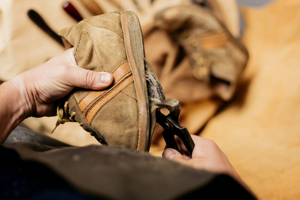 Cobbler repairing an old leather shoe. Male shoemaker using pliers on dirty boot's sole removing.  - Zdjęcie, obraz
