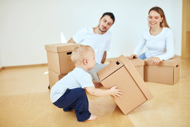little boy carrying moving box, parents on blurred background. Moving concept - 写真・画像