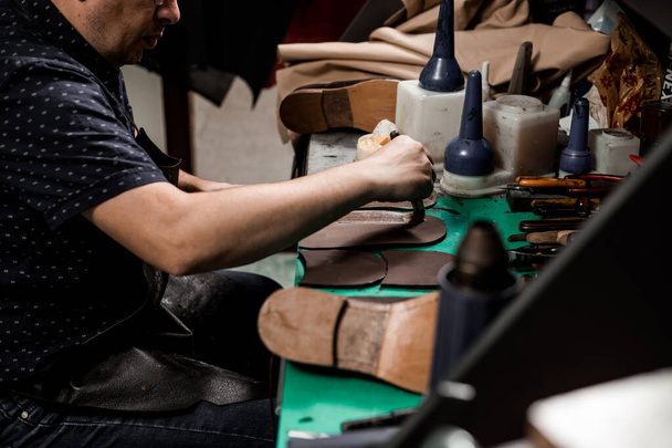 Cordonnier mâle assis à son magasin et réparer la chaussure de l'homme, brossant de la colle sur une nouvelle semelle. Look vintage. - Photo, image