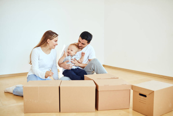 Family with boy unpacking moving cardboard boxes at new home - Фото, изображение