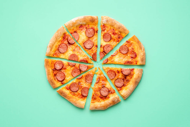 Sopra vista con pizza piccante tagliata a fette isolata su fondo verde menta. Posa piatta con un salame di pizza fatto in casa. - Foto, immagini