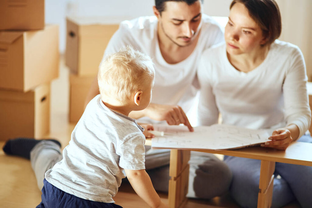 family reading instruction and assemble furniture together at living room of new apartment pile of moving boxes on background - Fotografie, Obrázek