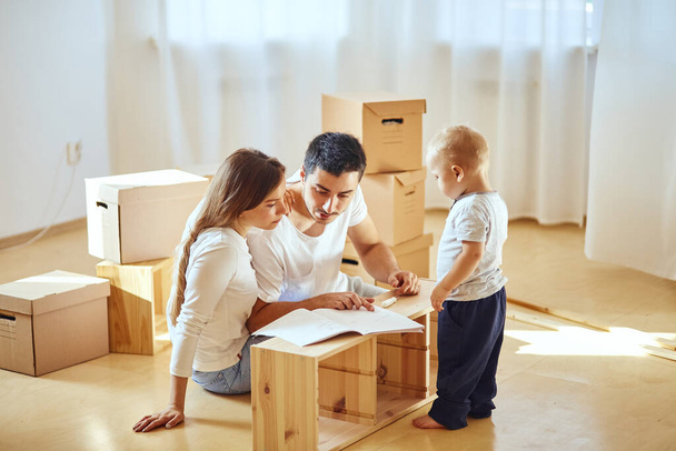 family reading instruction and assemble furniture together at living room of new apartment pile of moving boxes on background - Fotoğraf, Görsel