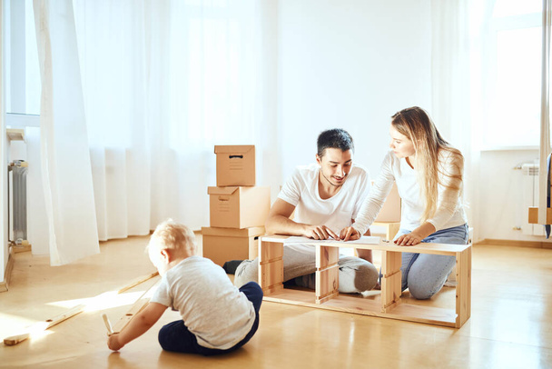 family together at living room of new apartment assembling furniture, pile of moving boxes on background - Fotoğraf, Görsel
