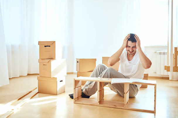 Concentrated man reading instructions to assemble furniture at home - Foto, Bild