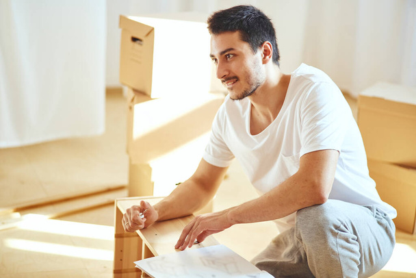 Concentrated man reading instructions to assemble furniture at home - Photo, Image