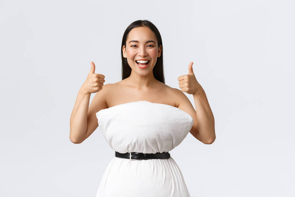 Szépség, divat és közösségi média koncepció. Boldog mosolygós ázsiai nő szórakozás részt vesz az internetes párna kihívás, hogy ruhát párna és öv cinching körül hulladék, mutasd hüvelykujj-up - Fotó, kép