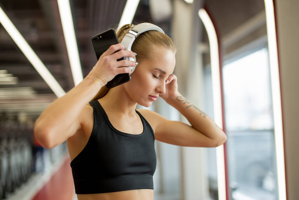 Sport and Music. woman hold headphones while working out in gym - Fotó, kép
