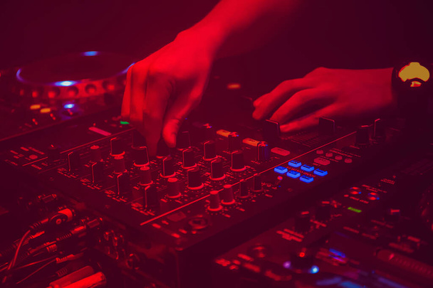 Ди-джей играет техническую музыку на столе с оборудованием в ночном клубе - Фото, изображение